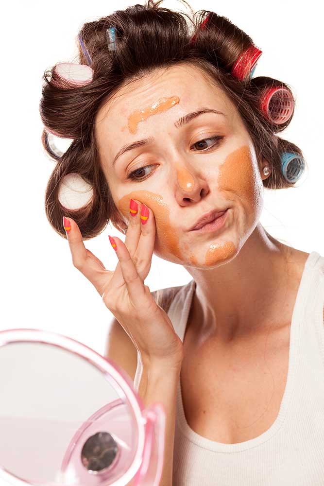 kobieta z wałkami na włosach nakładająca podkład na twarz